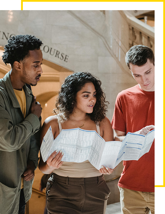 Three students collaborating and discussing a map or brochure.